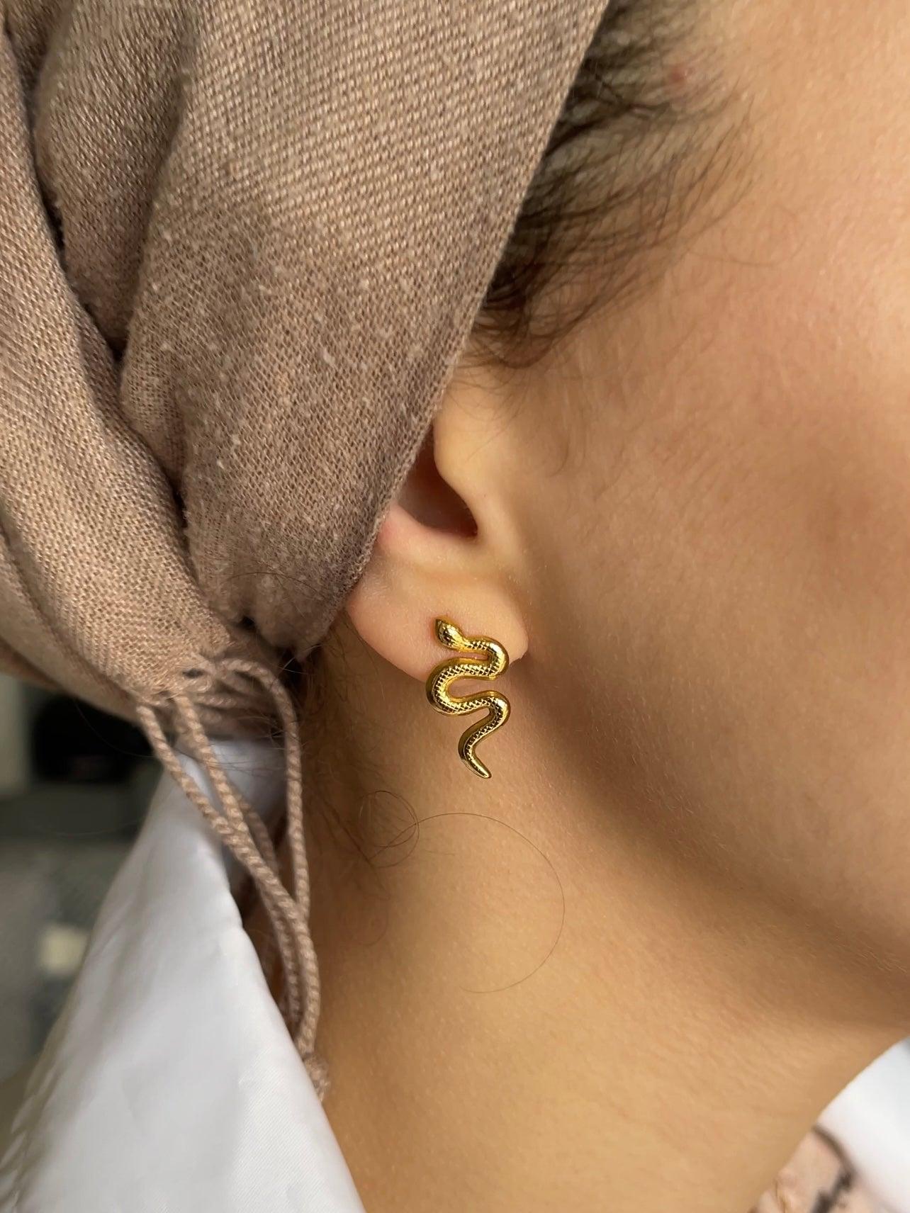 Close up on ear with 18k gold tiny small medusa snake reptile shape stud fashion jewelry earrings - Roulette Safari