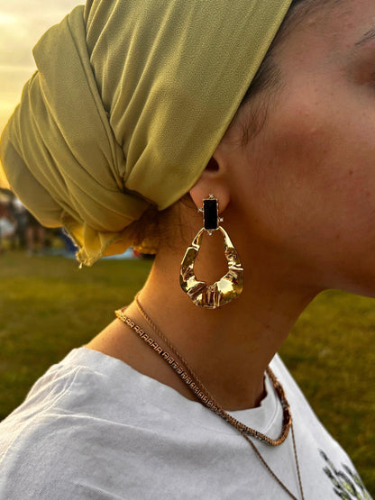 Close up on ear with maya Aztec gold and black tear rain drop shape dangle drop fashion jewelry earrings - Roulette Safari