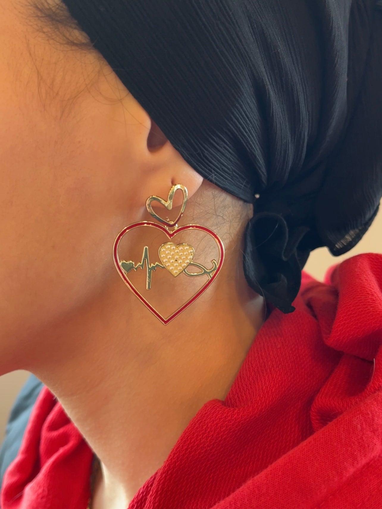 Close up on ear with red and gold ECG heartbeat asymmetric heart shape charm dangle drop fashion jewelry earrings - Roulette Safari