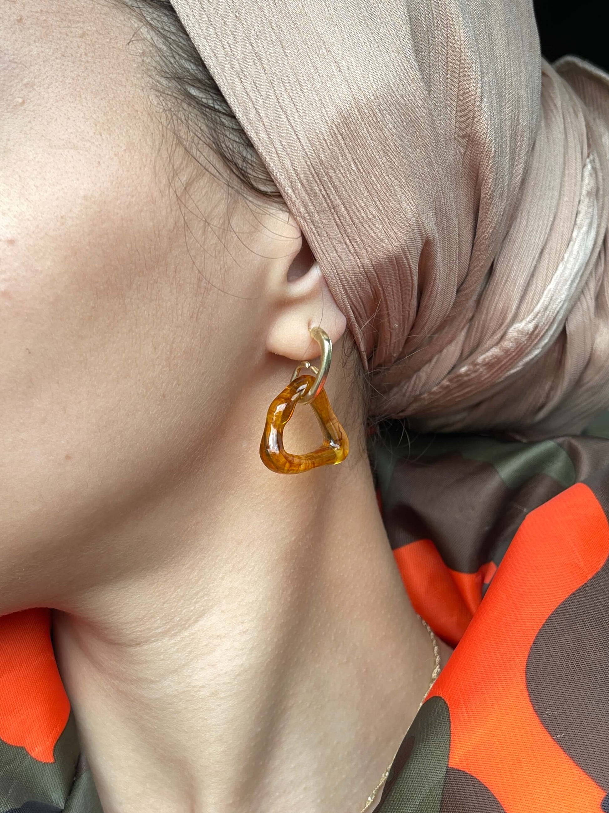 Close up on ear with amber abstract asymmetric triangle shape dangle drop resin fashion jewelry earrings - Roulette Safari