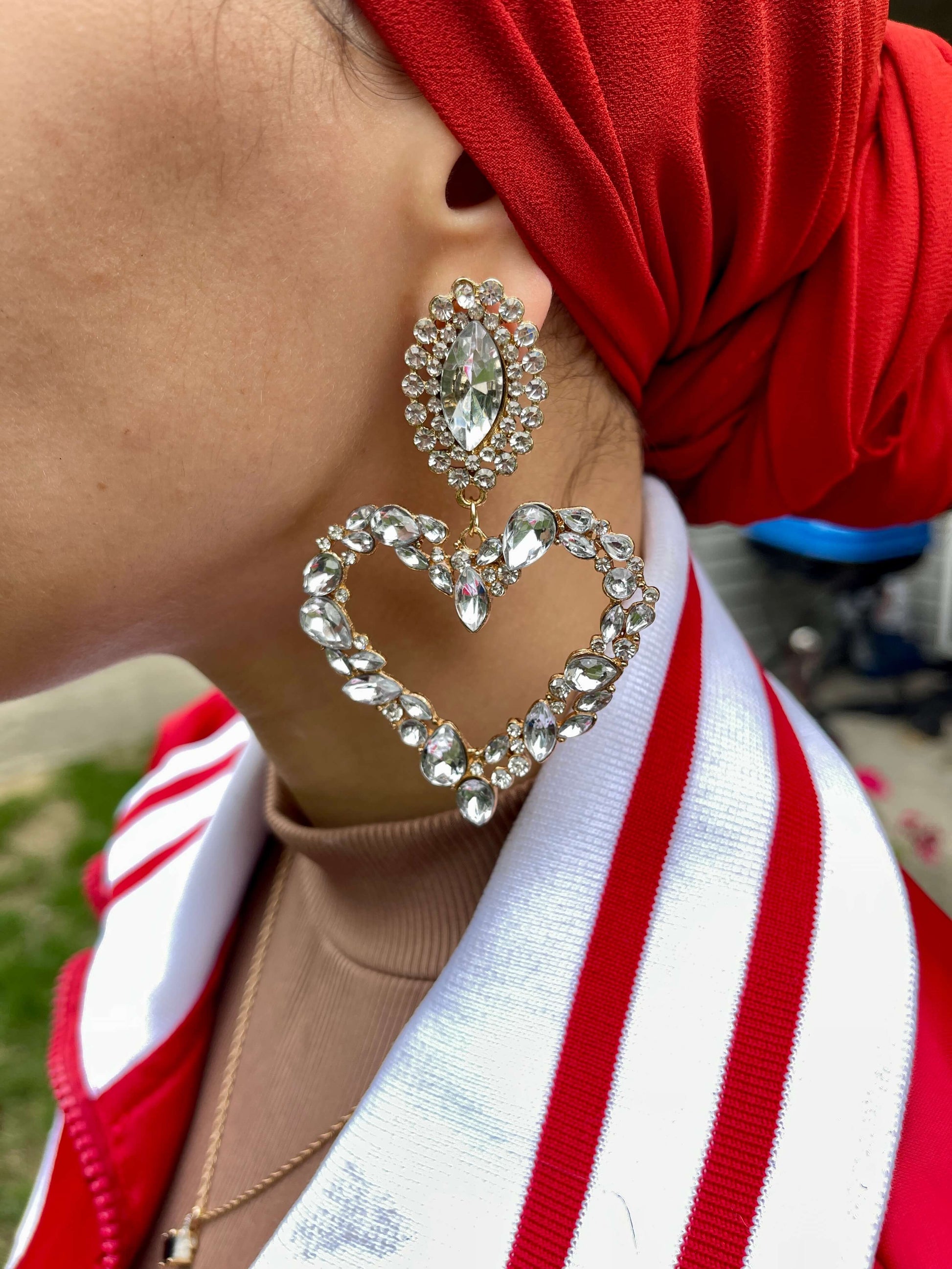 Close up to ear with white silver fancy heart shape dangle drop fashion jewelry earrings with rhinestones - Roulette Safari